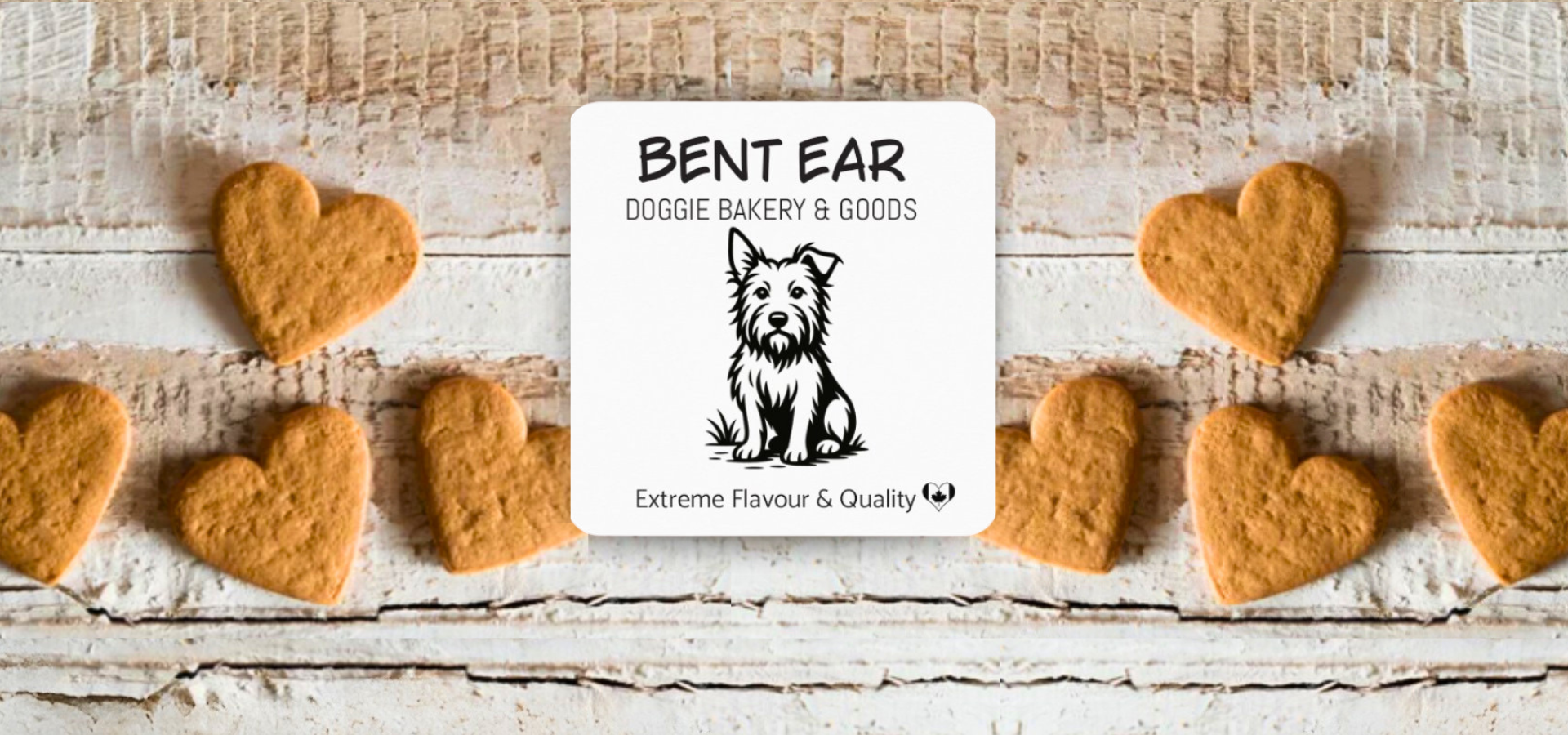 Heart-shaped dog cookies with Bent Ear Doggie Bakery & Goods sign on a wooden surface